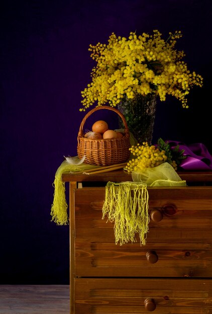 La Pasqua ancora in vita Uova in un cesto di vimini un bouquet di mimosa e candele della chiesa sul comodino in legno primo piano