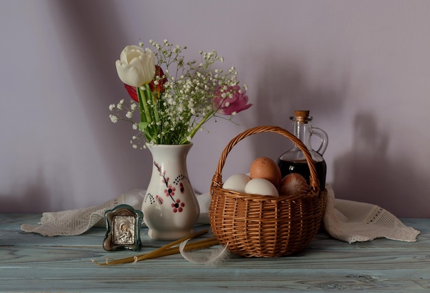 La Pasqua ancora in vita Uova in un cesto di vimini un bouquet di tulipani icona e candele della chiesa sul tavolo di legno primo piano