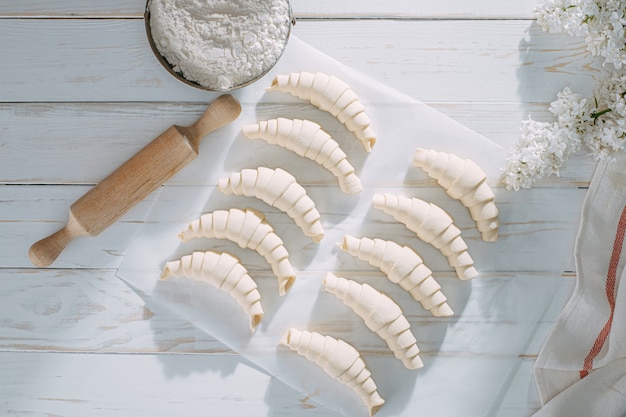 La pasta croissant rotolata e aspetta per cuocere su una tavola di legno bianca sul sole della carta di cottura di mattina