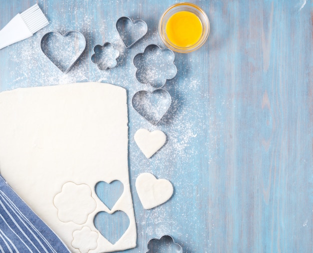 La pasta cruda della pasta sfoglia si trova sulla tavola di legno blu. Figure in metallo stampato