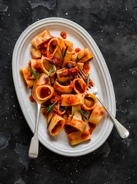 La pasta Paccheri con salsa di pomodoro e rosmarino è un delizioso pranzo vegetariano su uno sfondo scuro