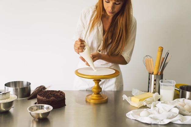 La pasticcera sta preparando un biscotto con crema bianca e torte da cucina al cioccolato