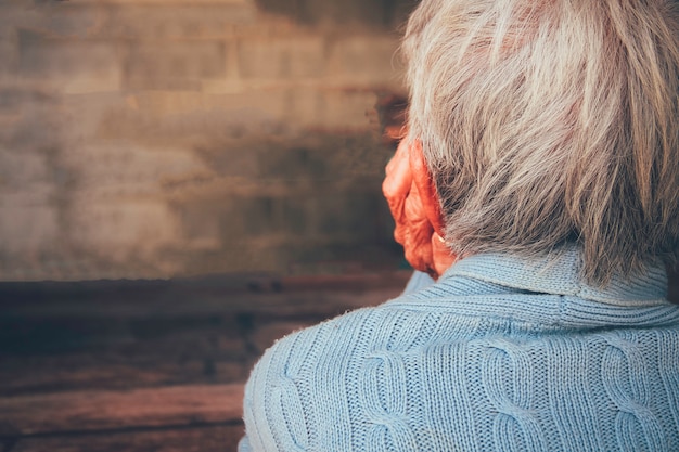 La persona anziana era triste e stressata. Sedeva con la mano appoggiata sul mento nella camera oscura. Concetto: demenza, solitudine drammatica, tristezza, depressione, delusione, abuso, assistenza sanitaria e dolore.