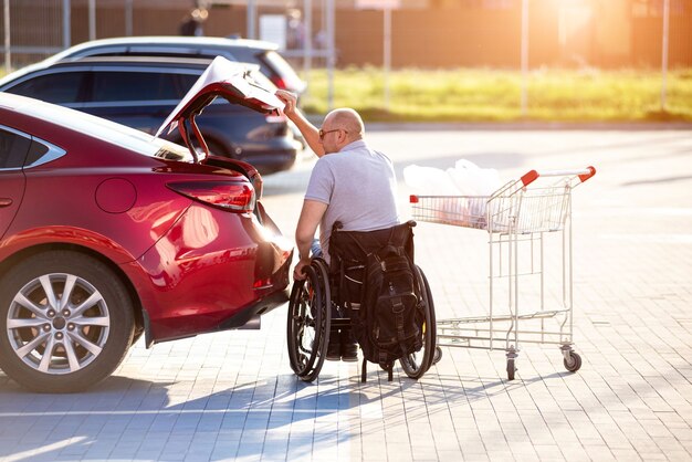 La persona con disabilità fisica mette gli acquisti nel bagagliaio di un'auto nel parcheggio di un supermercato