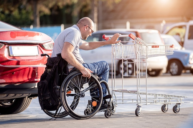 La persona con disabilità fisica mette gli acquisti nel bagagliaio di un'auto nel parcheggio di un supermercato