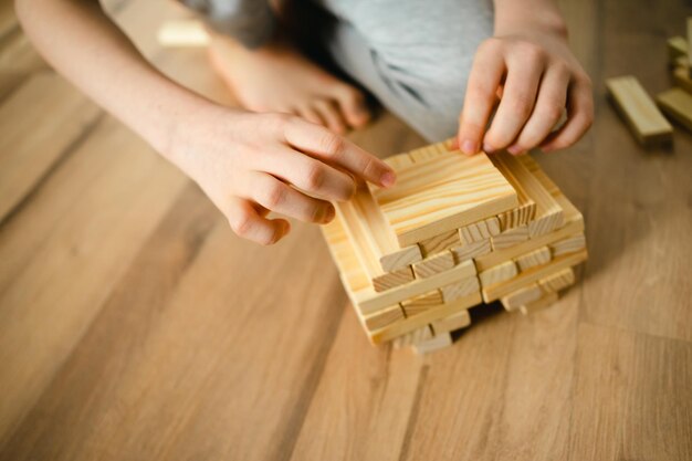 la persona del primo piano impila i blocchi di legno del progettista sul pavimento le mani dei bambini Giochi da tavolo e