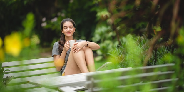 La persona della giovane bella donna è felice e si diverte con una bevanda al caffè al mattino a casa rilassa lo stile di vita tenendo una tazza di caffè o tè al parco naturale all'aperto sorride bella ragazza con il tempo della libertà