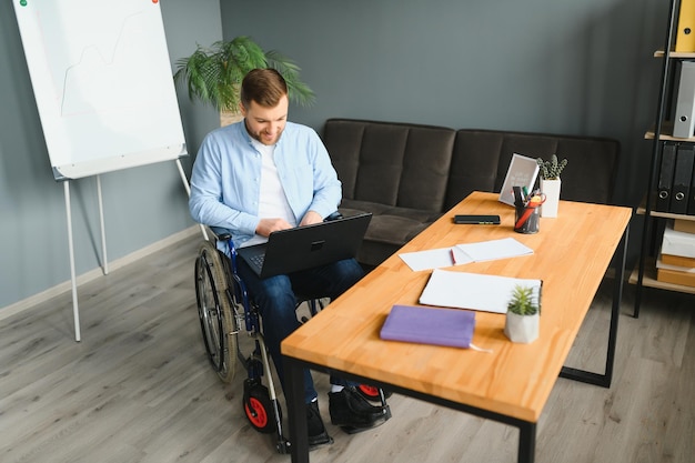 La persona disabile sulla sedia a rotelle lavora in ufficio al computer È sorridente e appassionato del flusso di lavoro