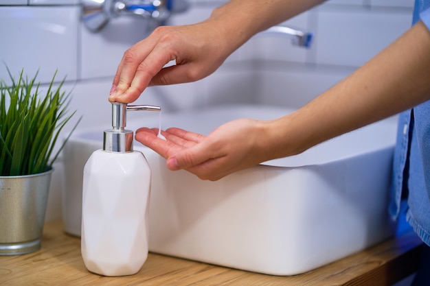 La persona si lava le mani nel lavandino del bagno con sapone liquido antibatterico. Protezione e prevenzione quotidiana da virus, microbi e batteri