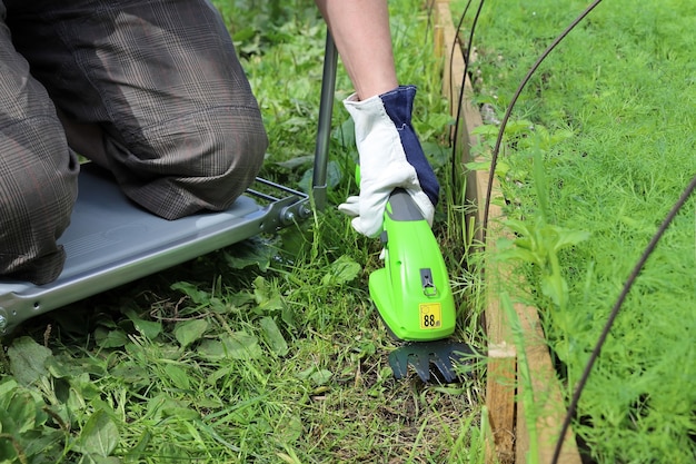 La persona taglia l'erba sul sentiero vicino al giardino con un trimmer elettrico portatile