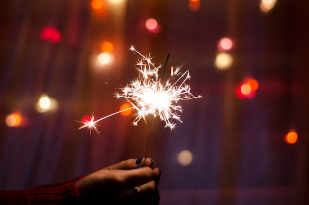 La persona tiene un bastone sparkler in una mano. Stelle filanti del festival. Felice anno nuovo.