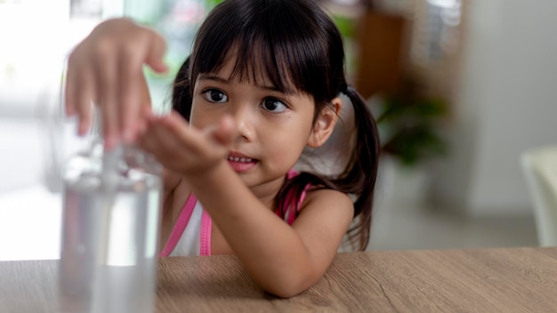 La piccola bambina asiatica ha messo la pompa igienizzante in gel alcolico sulle mani per pulirsi o lavarsi le mani