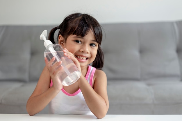 La piccola bambina asiatica ha messo la pompa igienizzante in gel alcolico sulle mani per pulirsi o lavarsi le mani