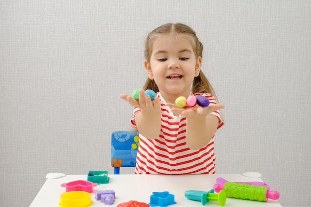 la piccola bambina sorridente in maglietta a righe gioca con la plastilina colorata a tavola bianca, gioca con la pasta a casa