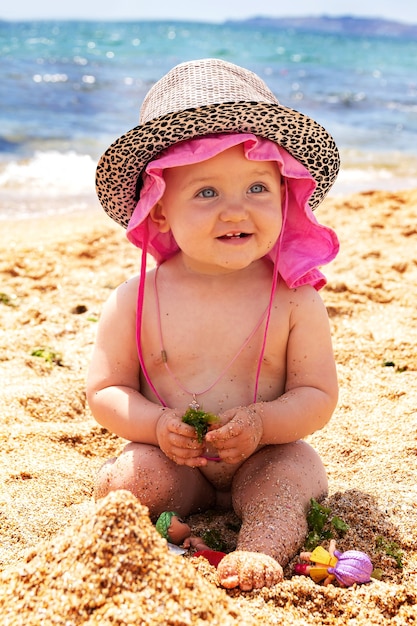 La piccola bambina sorridente sta giocando sulla spiaggia nella sabbia con i giocattoli Il bambino sta prendendo il sole al sole