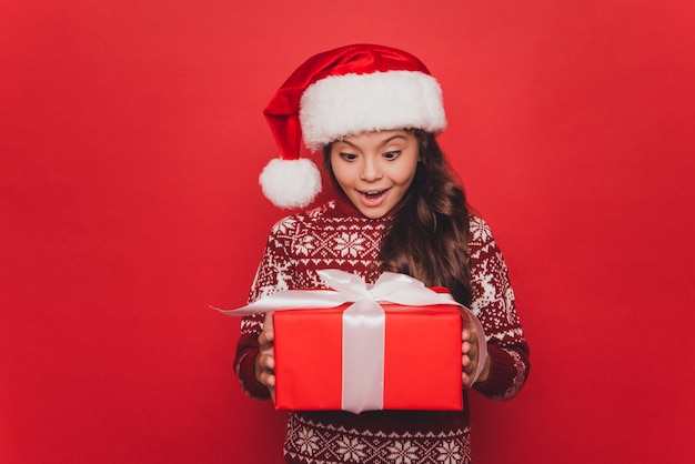 La piccola donna in vestiti lavorati a maglia di Natale tiene il contenitore di regalo