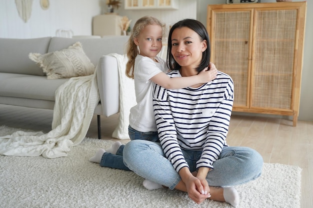 La piccola figlia adottiva abbraccia la madre seduta sul pavimento caldo a casa Buona maternità Mother39s Day