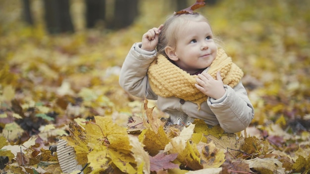 La piccola figlia gioca con le foglie gialle nel parco autunnale, la ragazza è felice e ride