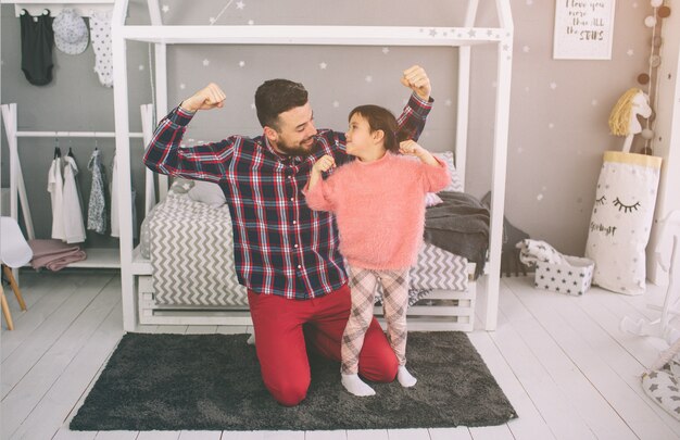 La piccola figlia sveglia e il suo bel giovane papà giocano insieme nella stanza del bambino. Papà e figlio trascorrono del tempo insieme seduti sul pavimento in camera da letto