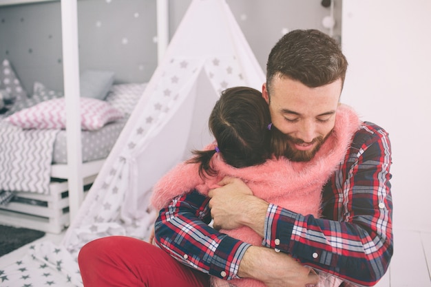 La piccola figlia sveglia e il suo bel giovane papà giocano insieme nella stanza del bambino. Papà e figlio trascorrono del tempo insieme seduti sul pavimento in camera da letto