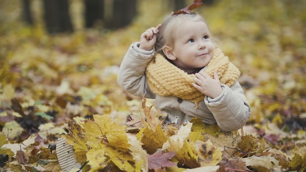 La piccola neonata felice gioca nel parco autunnale tra foglie gialle, teleobiettivo