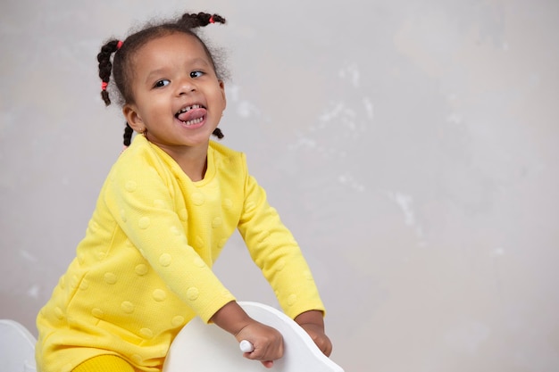 La piccola ragazza afroamericana in vestiti gialli mostra la lingua Bambino divertente