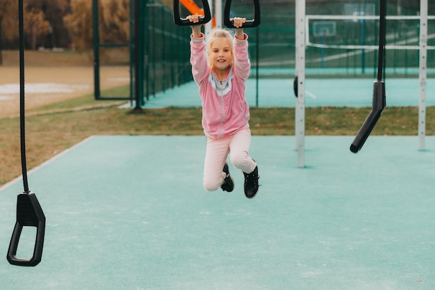 La piccola ragazza allegra gioca nel parco giochi. Il bambino è impegnato su anelli di ginnastica per strada. Il bambino pratica sport sui simulatori.