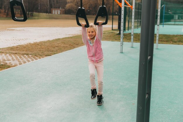 La piccola ragazza allegra gioca nel parco giochi. Il bambino è impegnato su anelli di ginnastica per strada. Il bambino pratica sport sui simulatori.