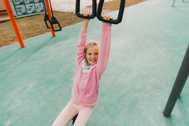 La piccola ragazza allegra gioca nel parco giochi. Il bambino è impegnato su anelli di ginnastica per strada. Il bambino pratica sport sui simulatori.