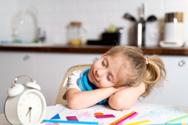 La piccola ragazza bionda a casa, stanca al tavolo della cucina, si è sdraiata con gli occhi chiusi