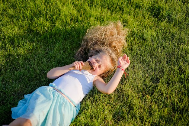 La piccola ragazza bionda con i capelli lunghi si diverte a mangiare il gelato in un parco estivo.