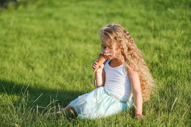 La piccola ragazza bionda con i capelli lunghi si diverte a mangiare il gelato in un parco estivo.