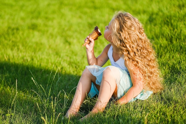 La piccola ragazza bionda con i capelli lunghi si diverte a mangiare il gelato in un parco estivo.