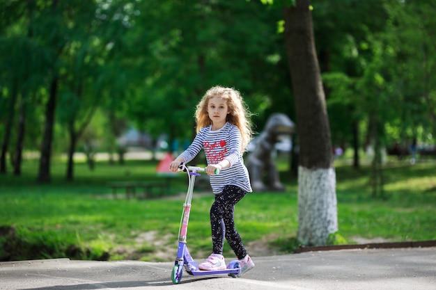 La piccola ragazza bionda guida lo scooter nel parco.