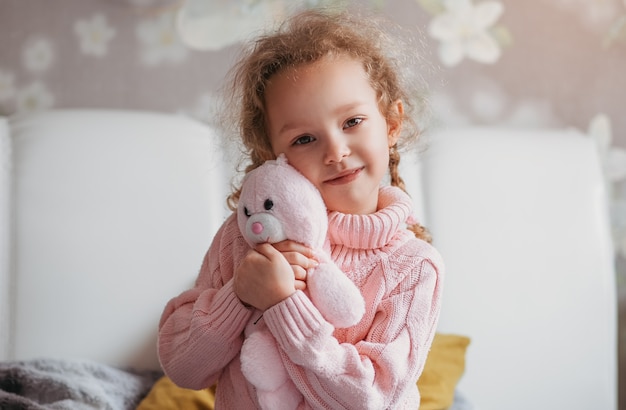 La piccola ragazza carina abbraccia un peluche in una stanza sul letto