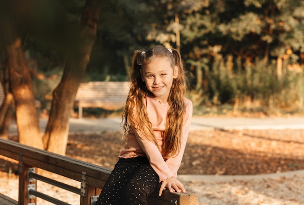 La piccola ragazza carina si siede su una panchina nel parco in autunno