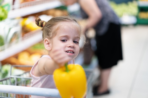 La piccola ragazza caucasica sceglie le verdure fresche nel supermercato.