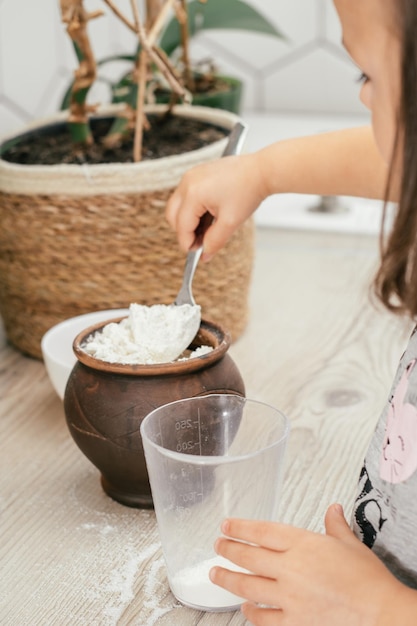 La piccola ragazza dai capelli scuri di 3 anni con la fascia rossa cuoce la torta di mele in cucina. Il bambino mette la farina nel misurino. I bambini aiutano nelle faccende domestiche. Kid cucinare cibo. Verticale