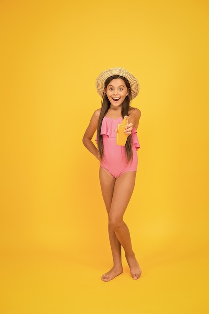 La piccola ragazza in costume da bagno tiene il concetto di abbronzatura sicura con crema cosmetica per la protezione solare