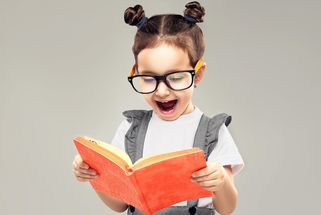 La piccola ragazza in età prescolare con un sorriso felice sul viso sta guardando in un grande libro con espressione di gioia