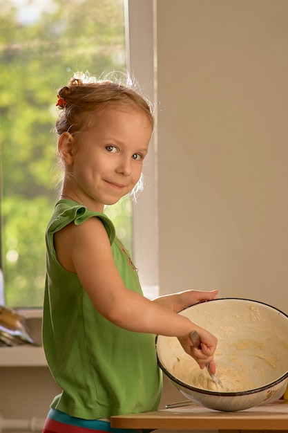 La piccola ragazza sveglia sta cucinando sulla cucina. Divertirsi mentre si fanno torte e biscotti.