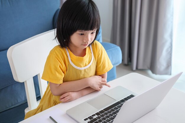 La piccola studentessa asiatica studia online utilizzando il computer portatile a casa