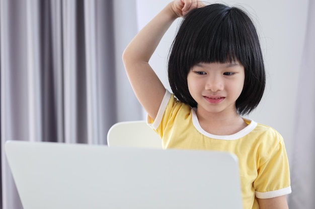 La piccola studentessa asiatica studia online utilizzando il computer portatile a casa