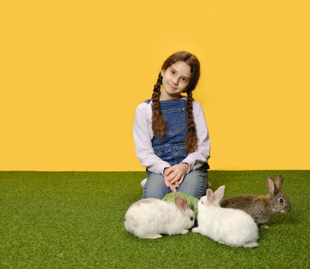 La piccola studentessa è sdraiata giocando con i conigli sullo sfondo giallo dello studio Copia spazio