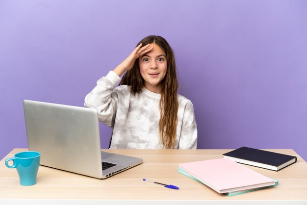 La piccola studentessa in un posto di lavoro con un laptop isolato su sfondo viola ha realizzato qualcosa e intendeva la soluzione