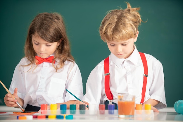 La pittura della ragazza e del ragazzo dei bambini della scuola con il colore e la spazzola delle pitture in aula.