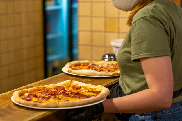 La pizza finita viene ritirata da una cameriera in mascherina e guanti della cucina da portare ai clienti