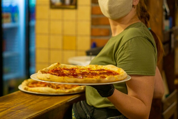 La pizza finita viene ritirata da una cameriera in mascherina e guanti della cucina da portare ai clienti