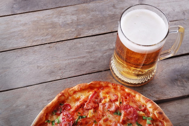 La pizza gustosa e il bicchiere di birra sono sul tavolo di legno da vicino.