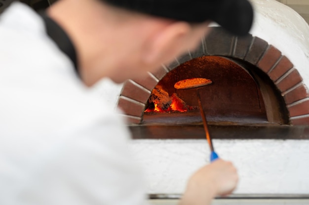 La pizza italiana è cotta in un forno a legna Il cuoco mette la pizza nel forno su una pala